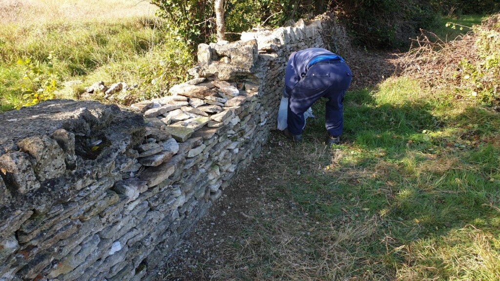 A person in blue pants bending over a stone wall

Description automatically generated